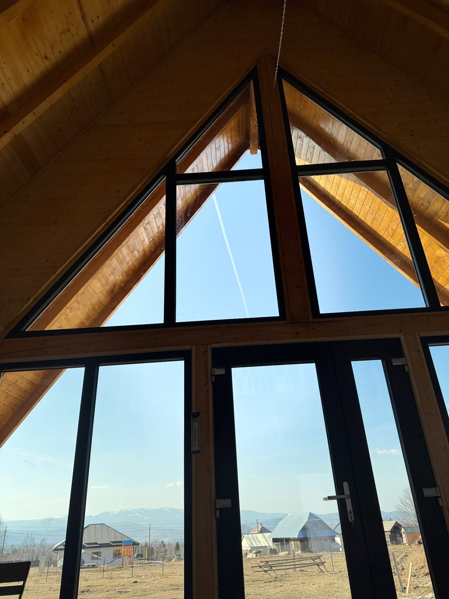 Vedere prin ferestrele A-frame ale cabanei catre peisajul din Apuseni